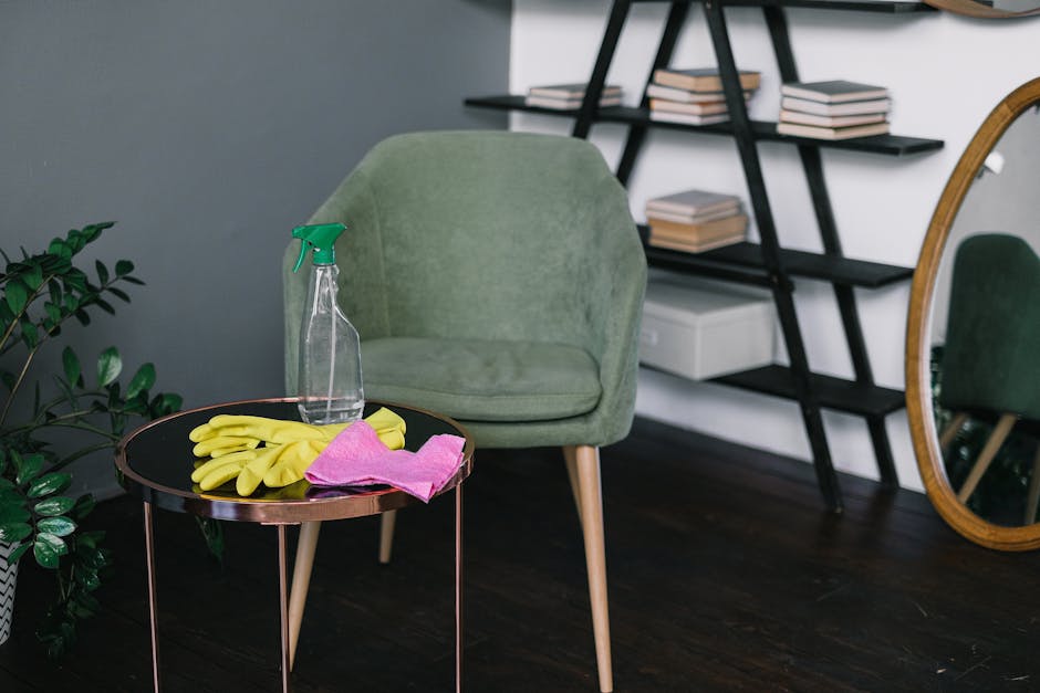 A light blue silicone wall hook mounted on a smooth, neutral grey wall, holding a wooden-handled scrubbing brush with stiff bristles and a beige cleaning cloth. The brush and cloth are neatly arranged