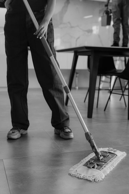 Three professional cleaners from Kennington Cleaners, wearing matching grey t-shirts and bright orange aprons, standing in a modern indoor space with a neutral grey wall and a window in the background